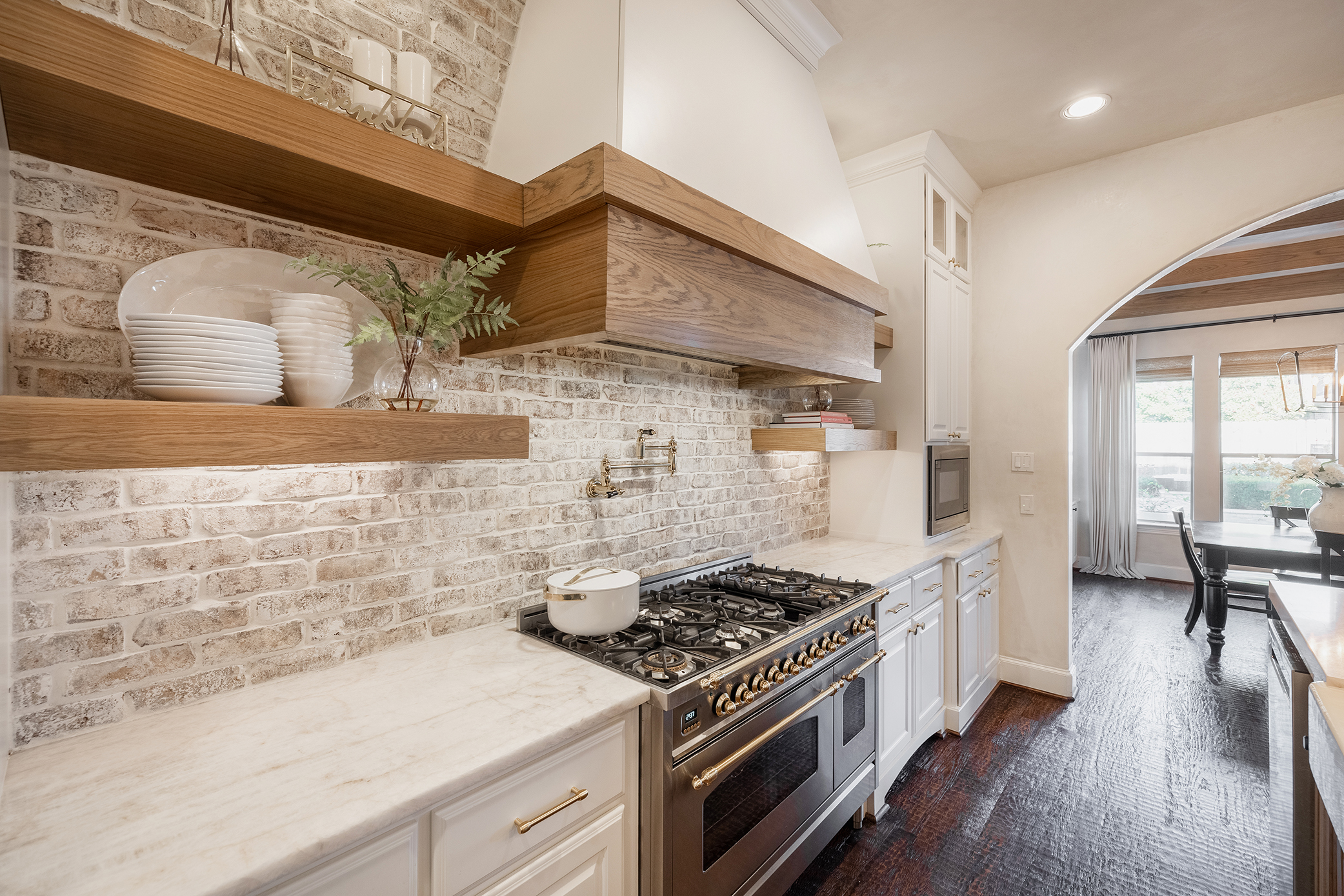 Decorating Den Interiors kitchen in Pickering, ON. Wooden accent range hood, stainless steel stove, marble counters, and brick backsplash.